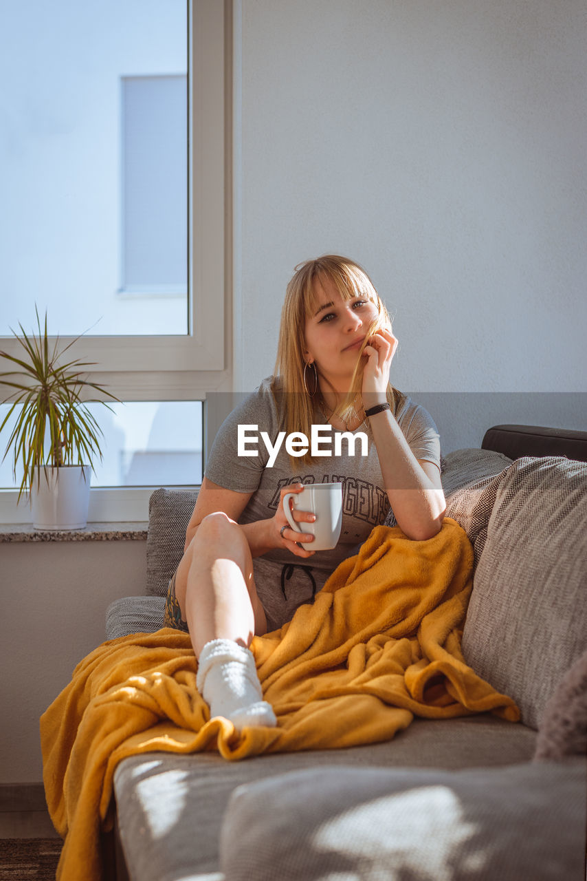 Woman with cup in hand and blanket on couch. 