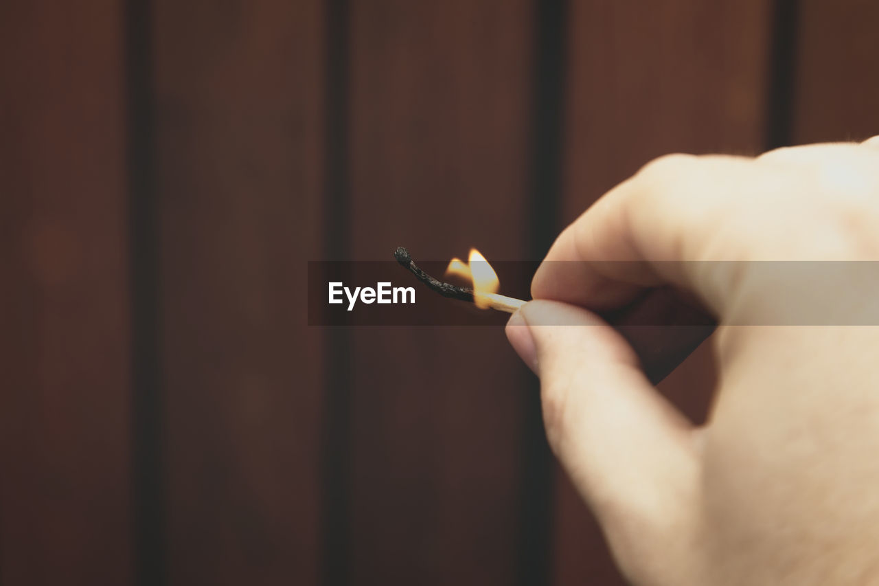 CLOSE-UP OF HAND HOLDING CIGARETTE AGAINST BLURRED BACKGROUND