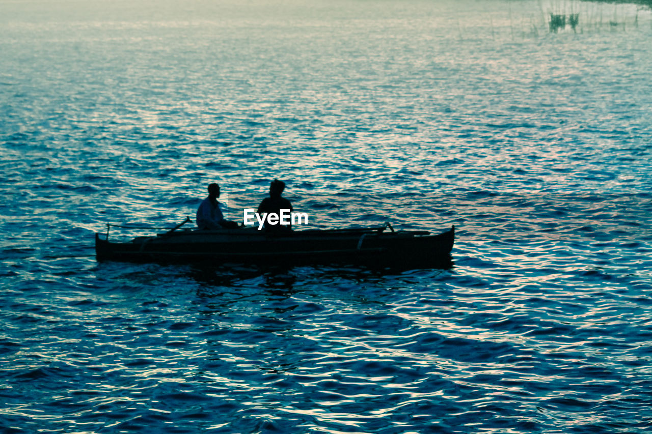 Silhouette people on boat in sea during sunset