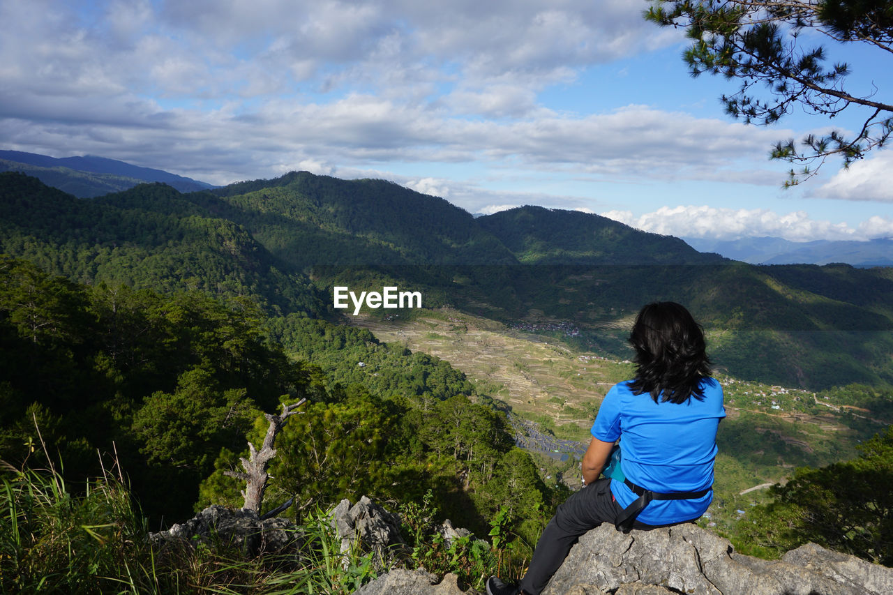 Rear view of woman sitting on mountain against sky
