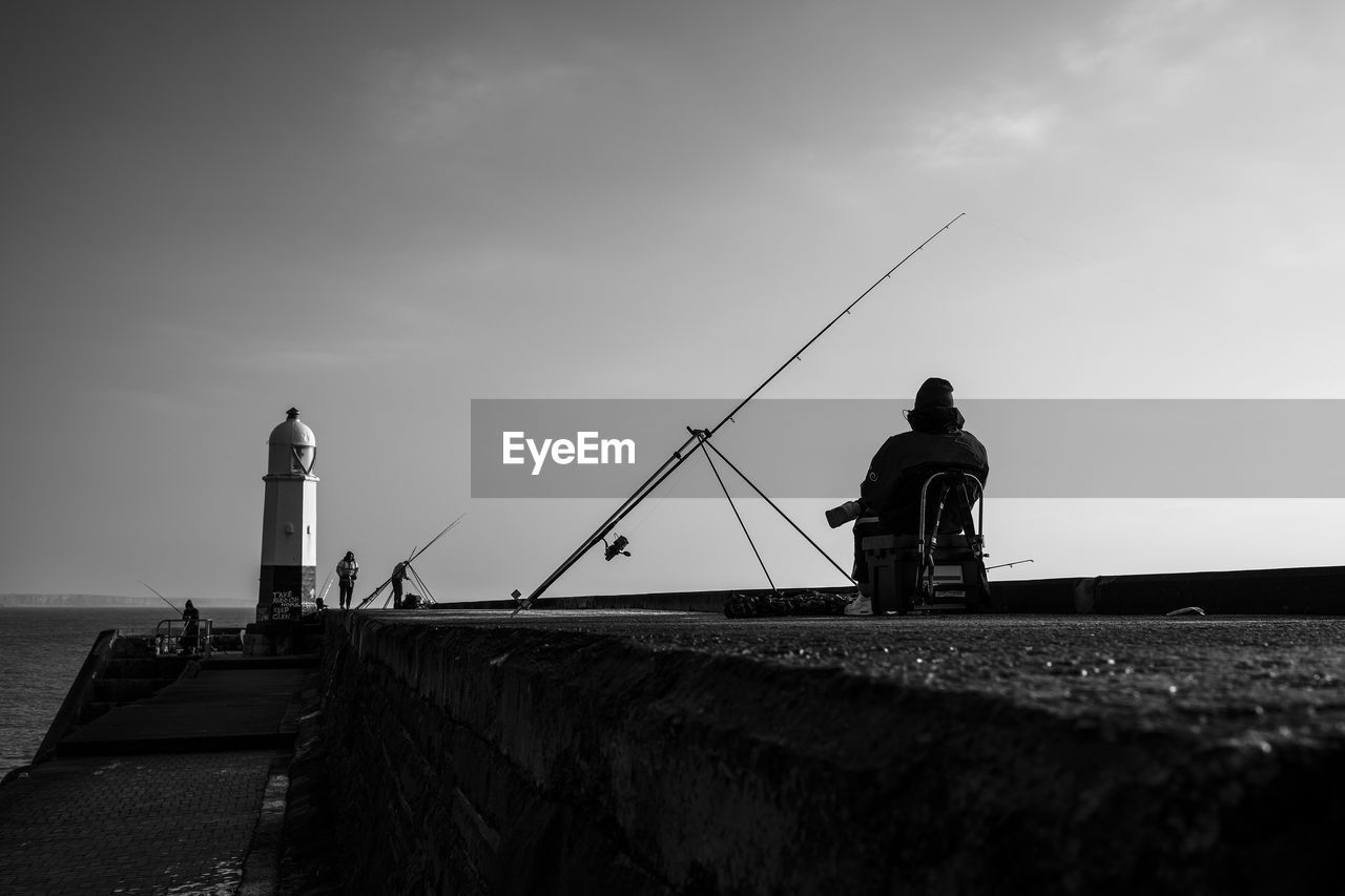 MAN STANDING ON LIGHTHOUSE BY WATER AGAINST SKY