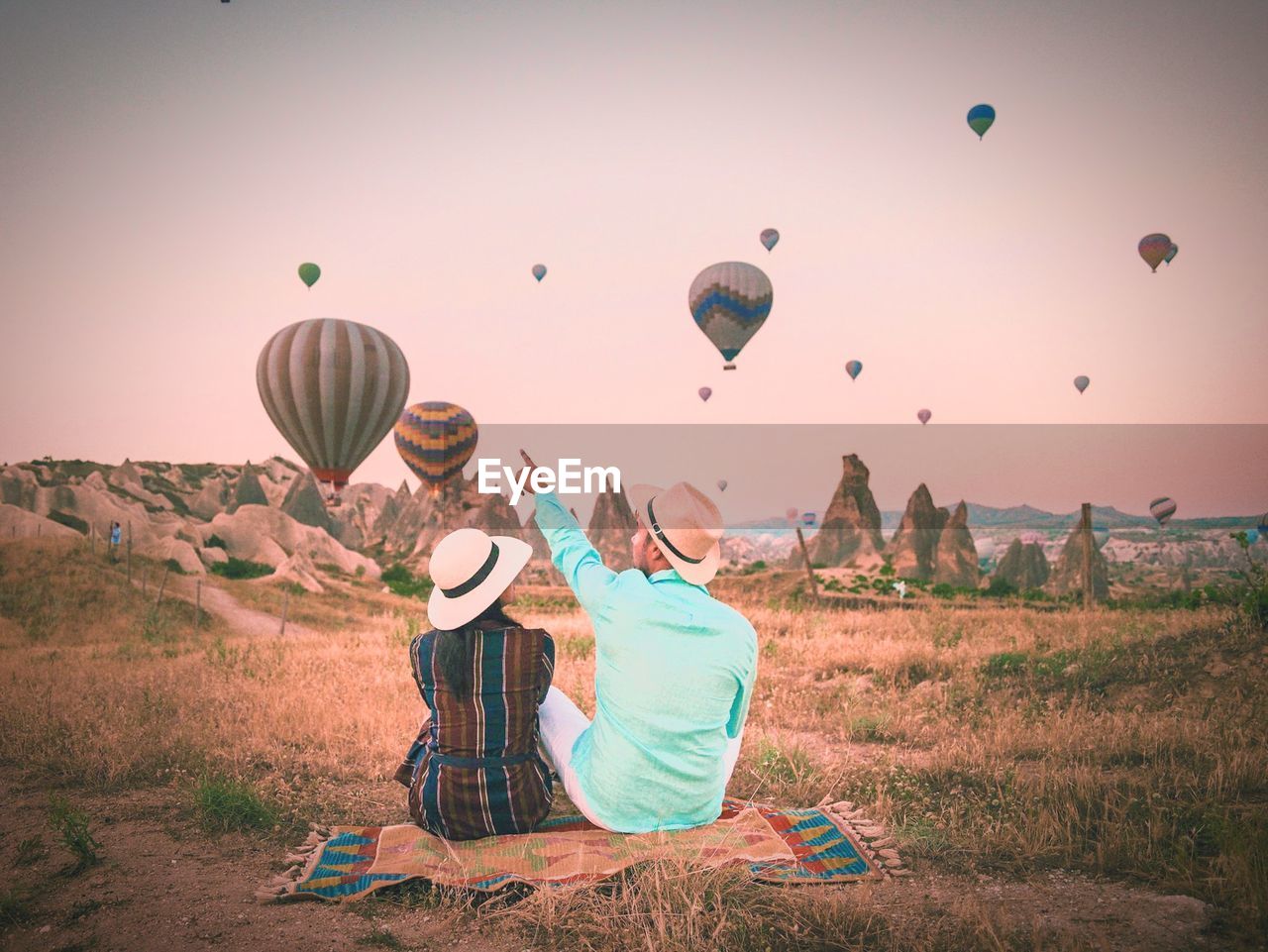 Couple looking at hot air balloons on field against sky