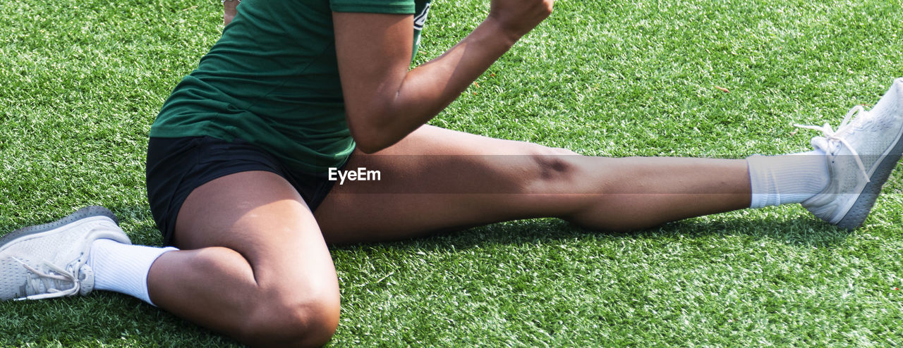 Close up of female athlete stretching in a hurdlers stretch on a green turf field.