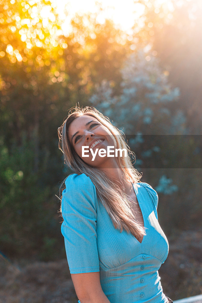 Smiling young woman standing in forest at sunset