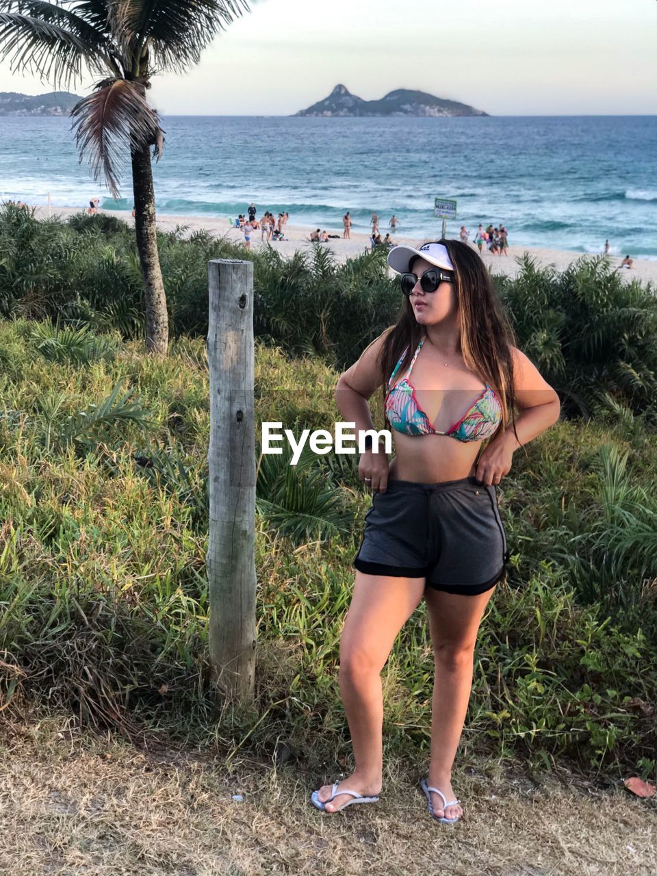 FULL LENGTH PORTRAIT OF YOUNG WOMAN STANDING ON SHORE