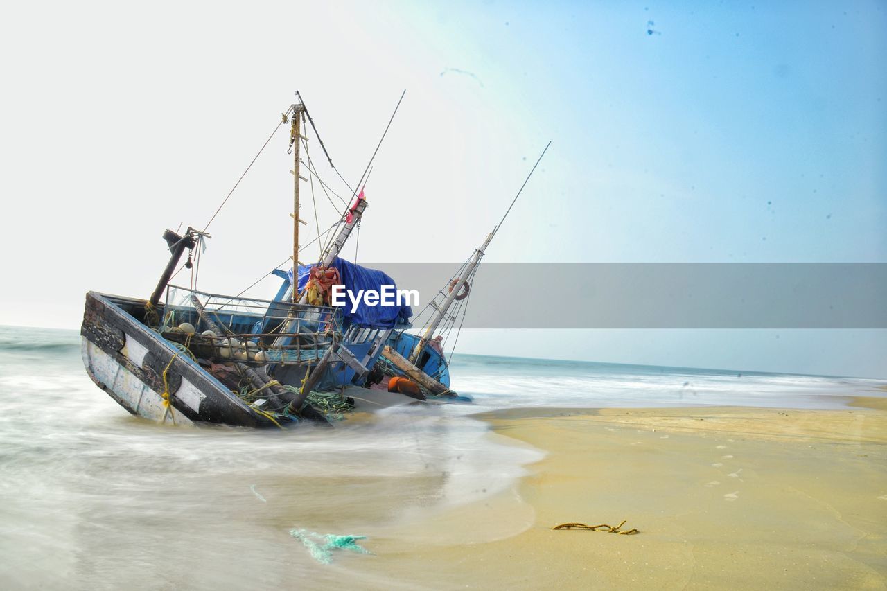 Fallen fishing ship at beach against clear sky