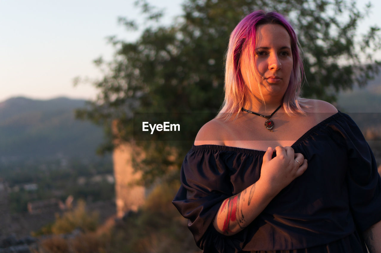 Young woman with dyed hair standing against trees