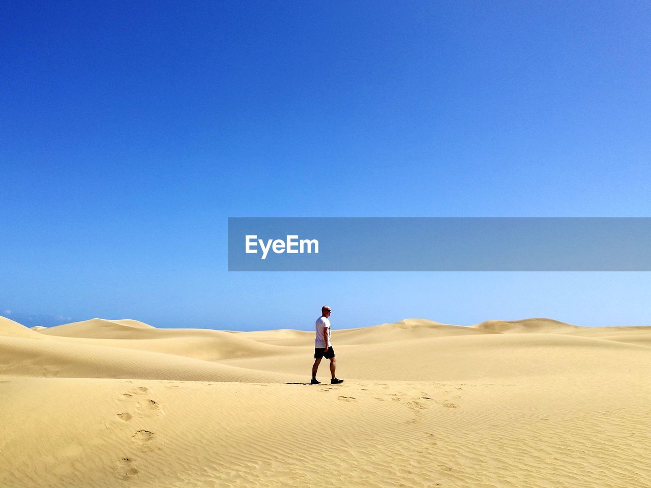 Man walking on desert against clear blue sky