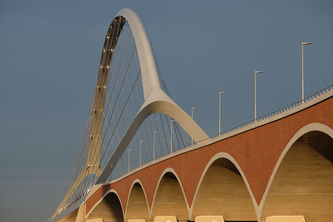 Low angle view of arch bridge against buildings against sky. 