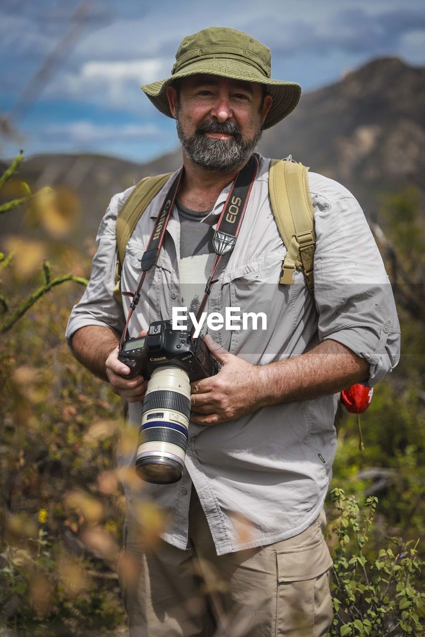 MIDSECTION OF MAN HOLDING CAMERA ON FIELD