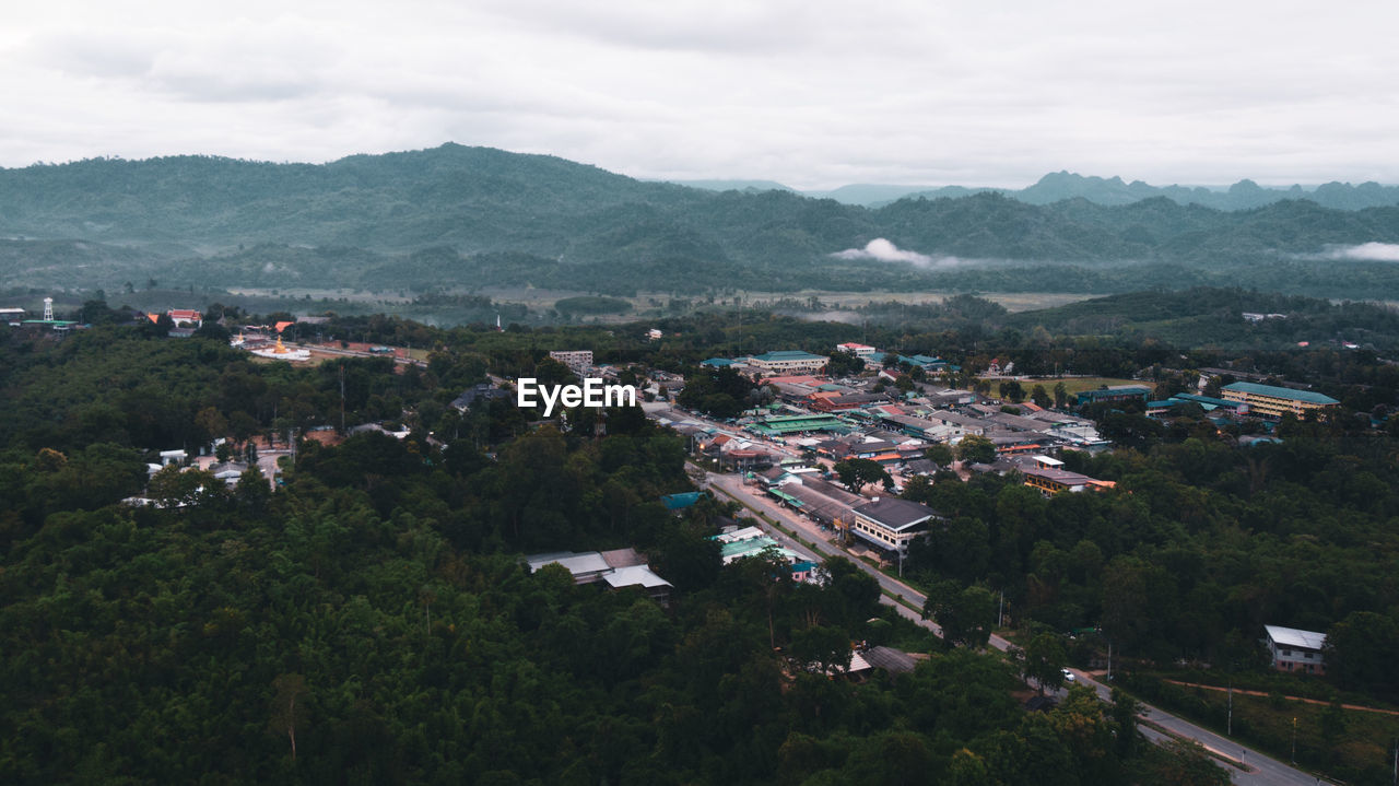 HIGH ANGLE VIEW OF TOWNSCAPE AND TREES BY MOUNTAIN AGAINST SKY