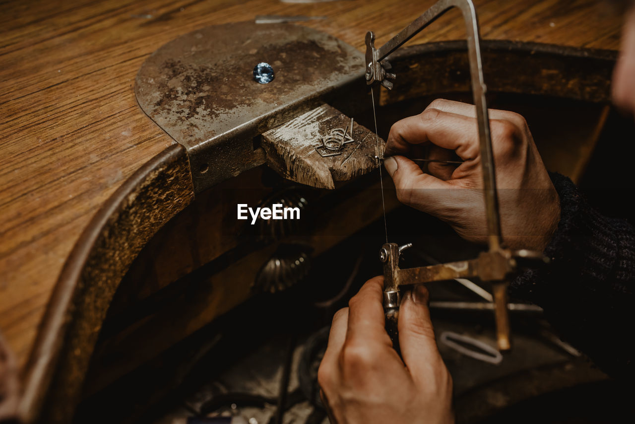 Goldsmith cutting metal with saw while making jewellery in workshop