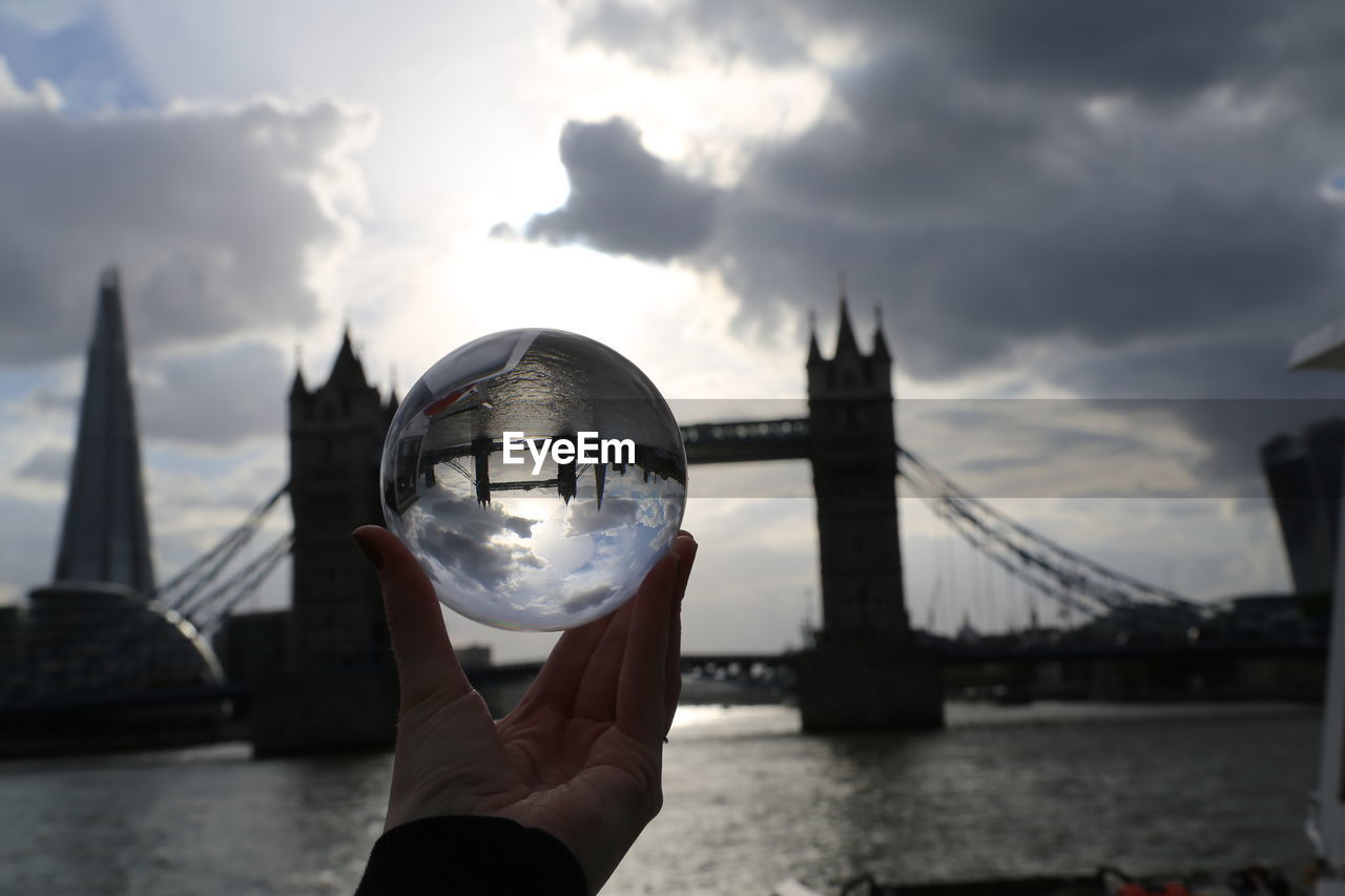 Cropped image of hand holding crystal ball with reflection of tower bridge