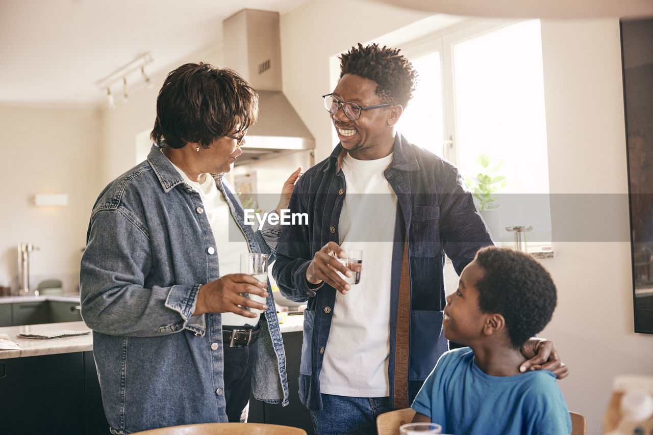 Senior woman with glass of water talking to son and grandson at home