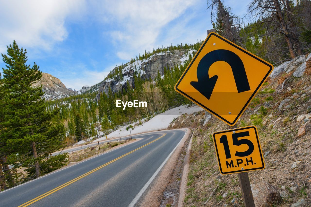 ROAD SIGN AGAINST TREES AND MOUNTAINS