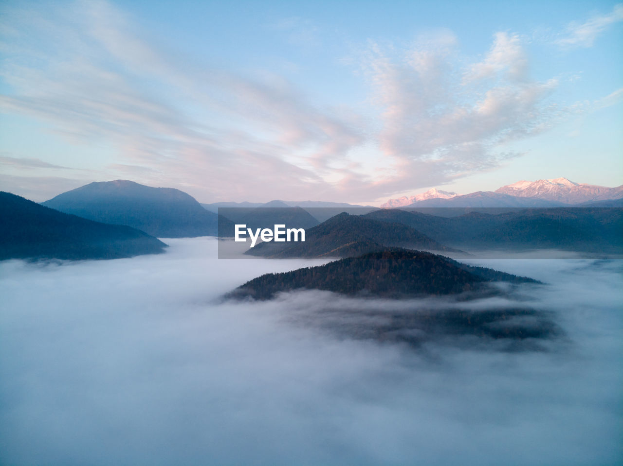 Aerial view, sea of fog and clouds illuminated by the rising sun, snow on the tops of the mountains