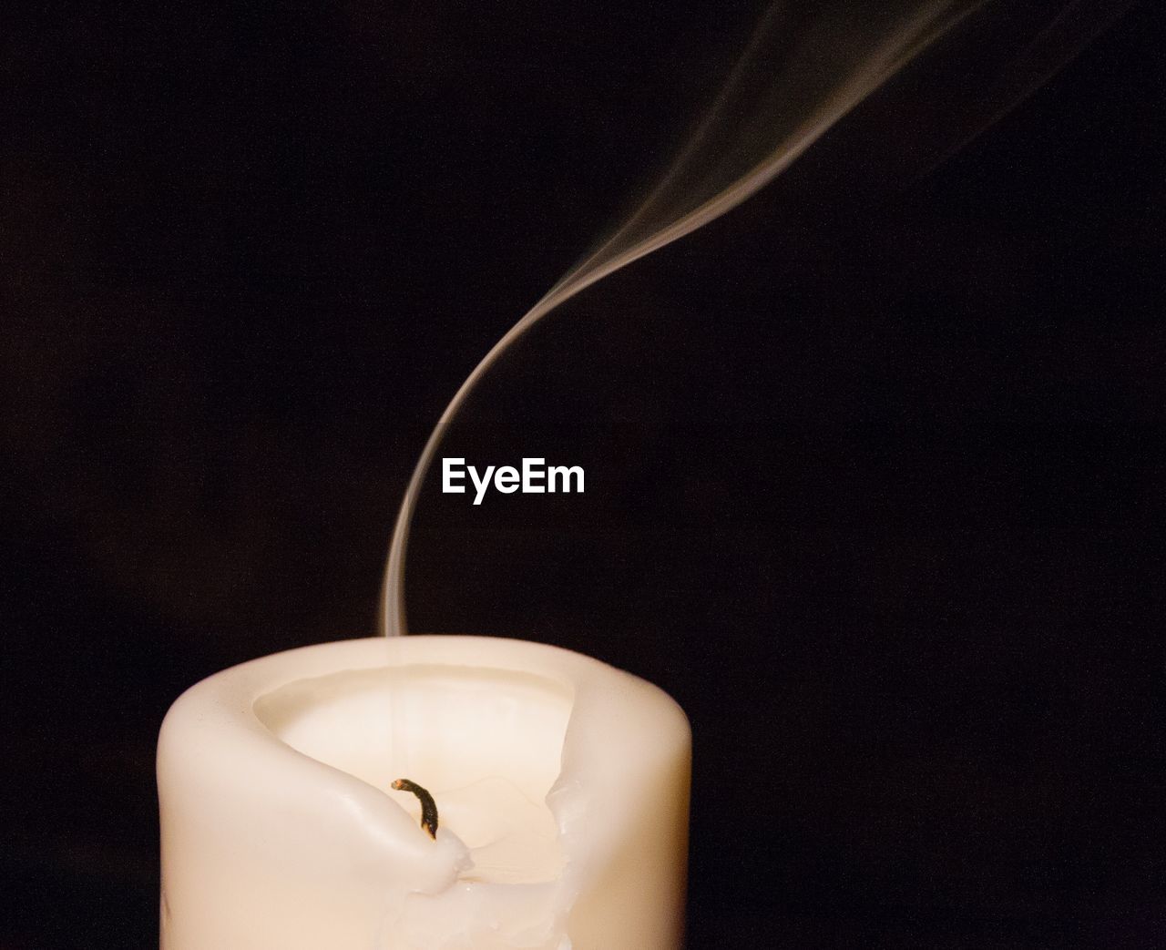 Close-up of smoke rising from extinguished candle against black background
