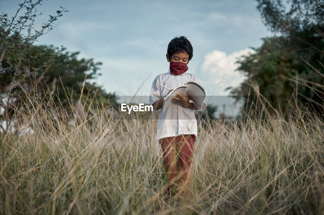 Boy standing reading a book in a meadow natural park. new normal education and learning concept