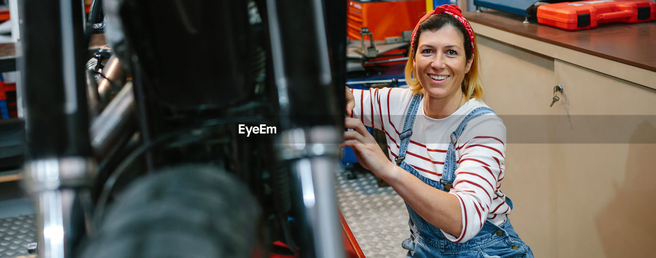 Portrait of mechanic woman repairing motorcycle on factory