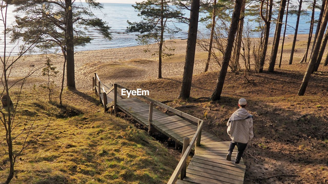 Rear view of man standing on boardwalk leading towards beach