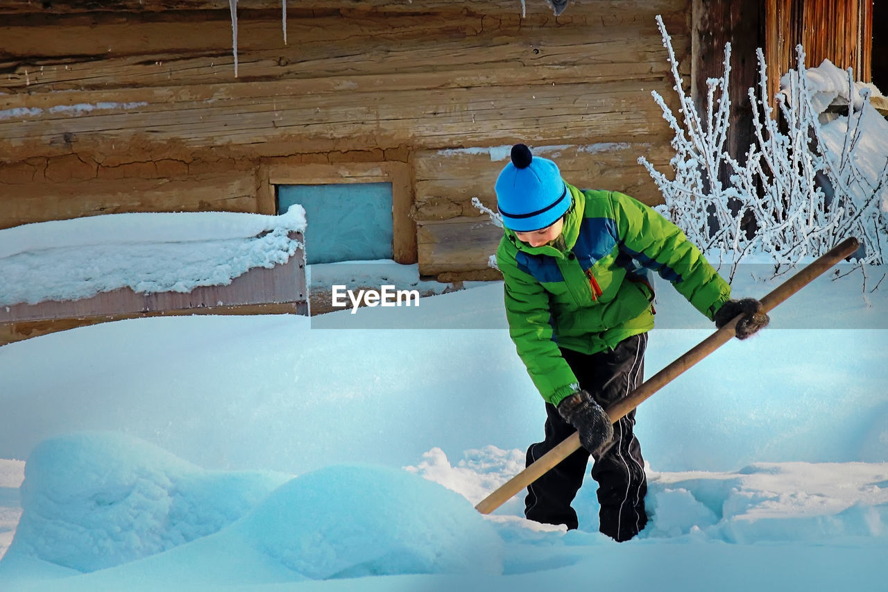 Boy cleaning snow outside cottage