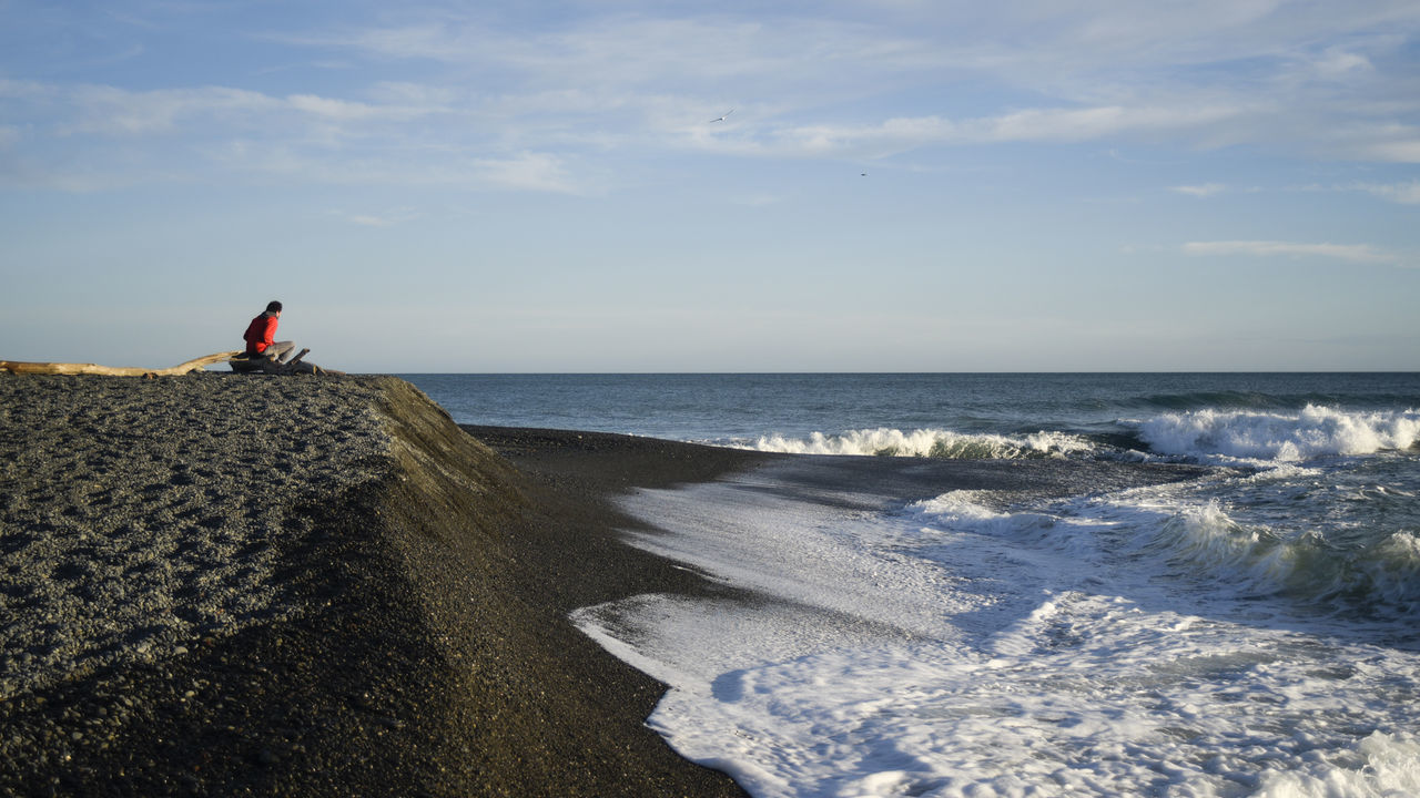 Person sitting on sea shore against sky