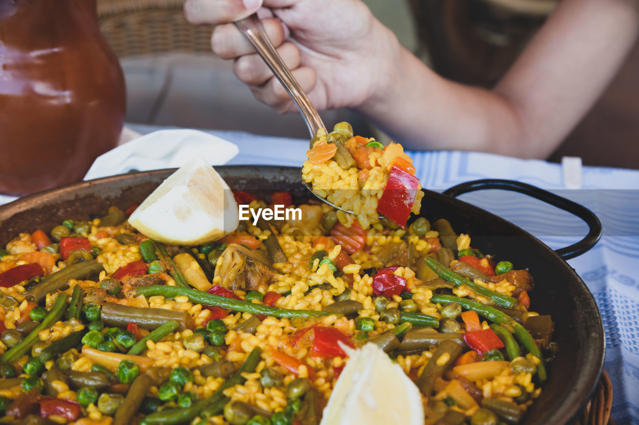 Vegan paella with rice and some vegetables. hand grabs a spoon with a portion.