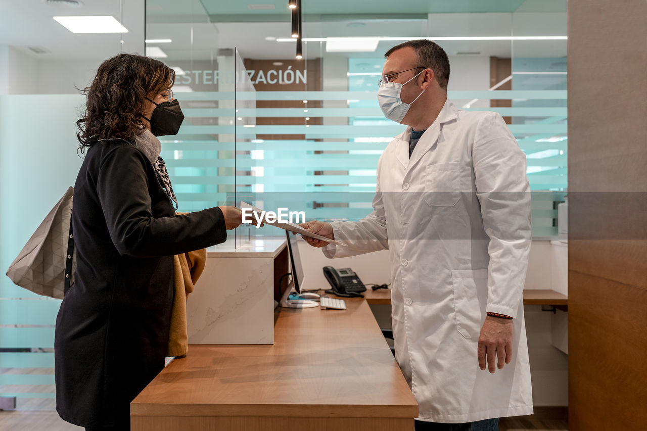 Doctor giving medical test report to patient at reception desk in pandemic