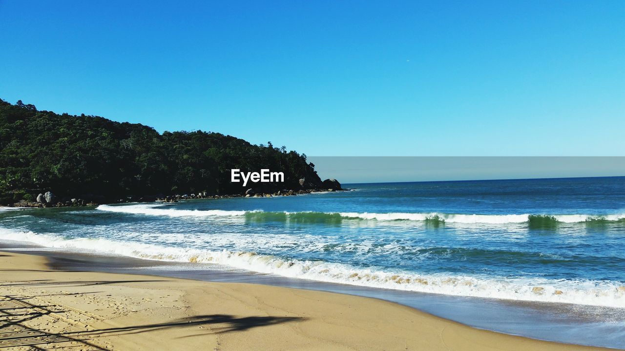 View of calm beach against clear blue sky