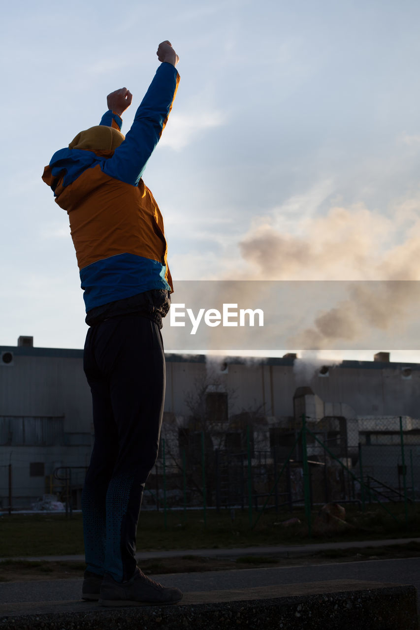 Full length of man stretching arms while standing against factory in city