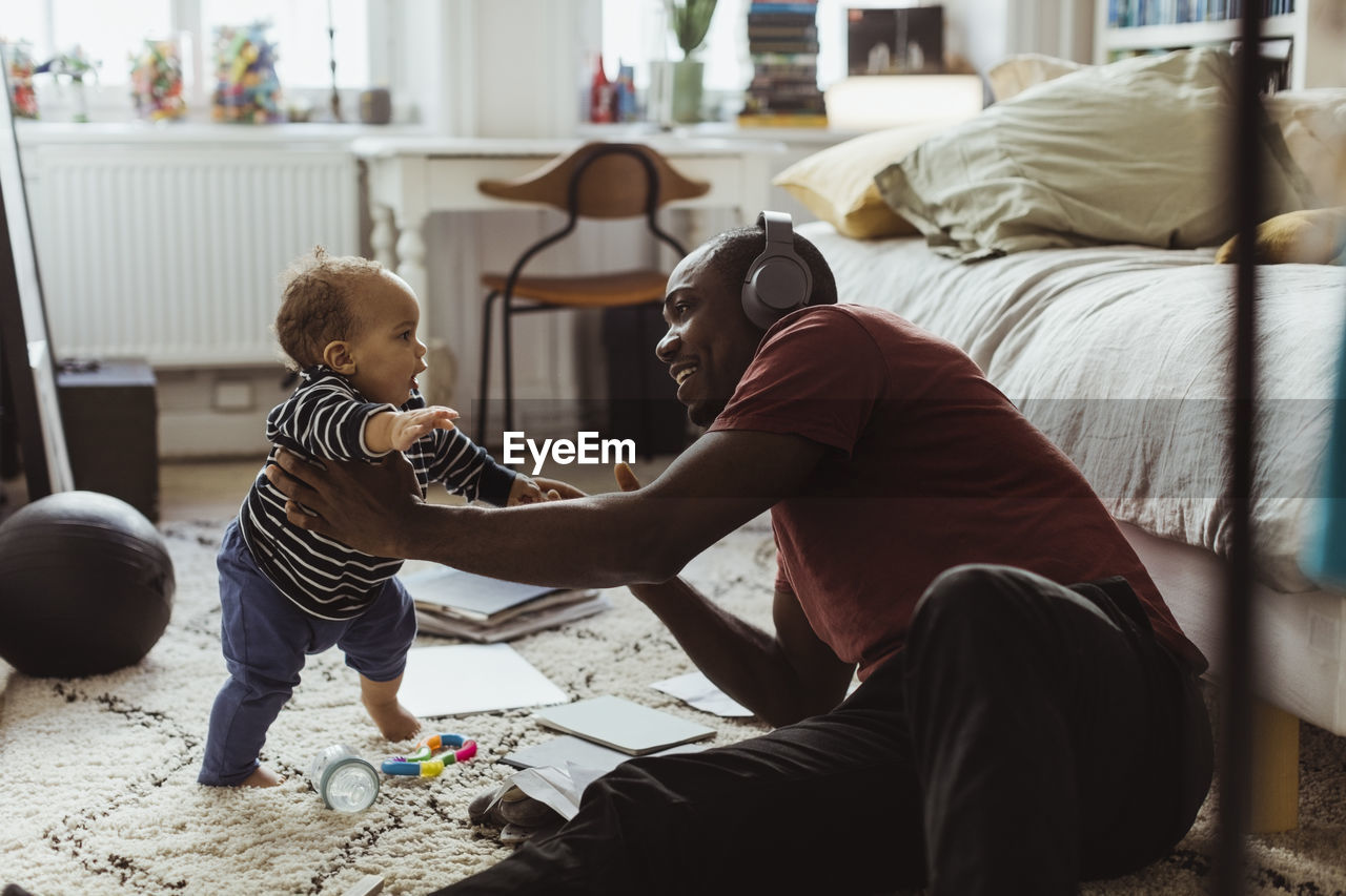 Father holding male toddler while sitting in bedroom at home