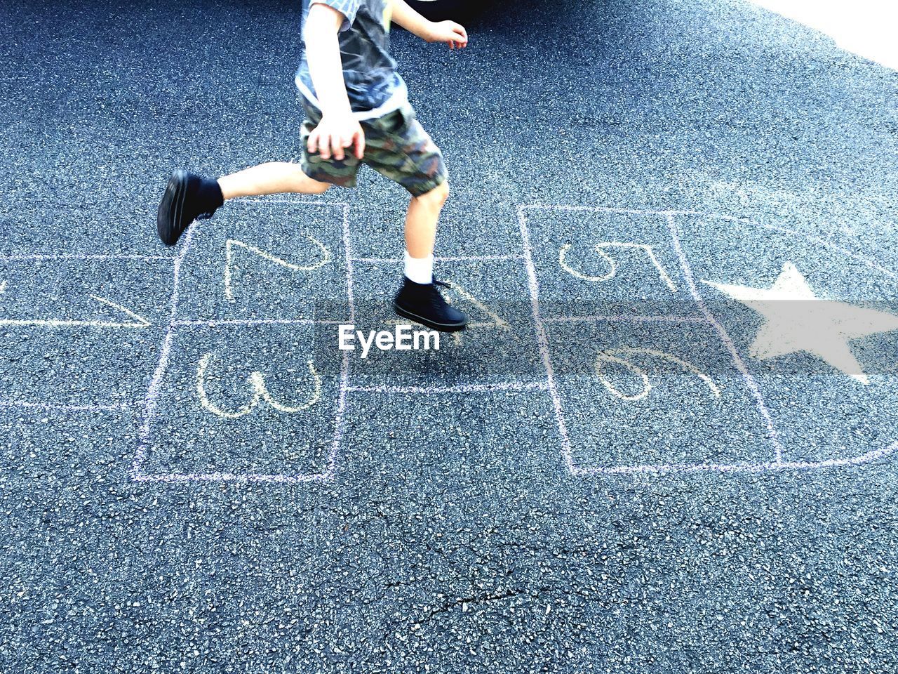 Low section of boy jumping on hopscotch