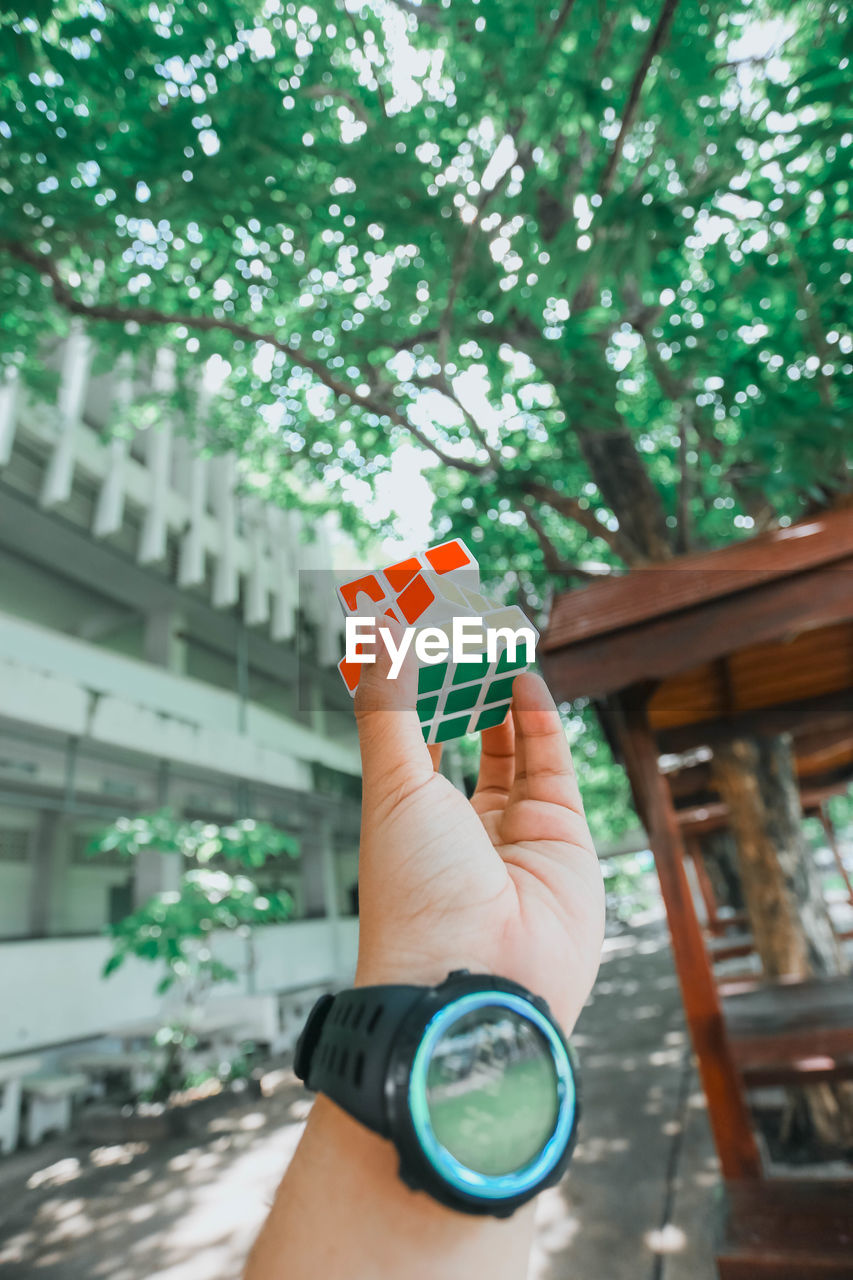 Cropped hand holding toy cube against trees