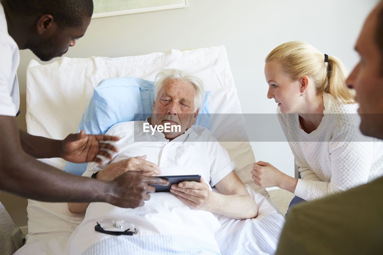 Male nurse showing digital tablet to senior man and couple at hospital ward