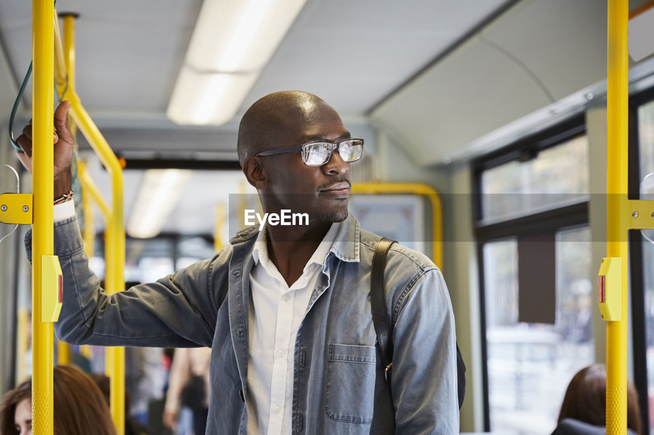 Confident male commuter looking away while standing in tram