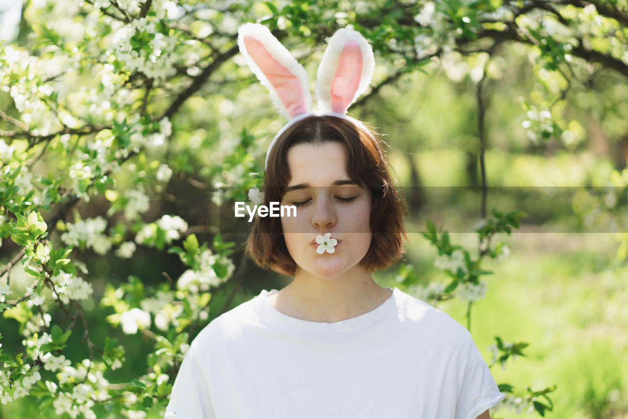 Funny teen girl with bunny ears on easter egg hunt in sunny spring garden