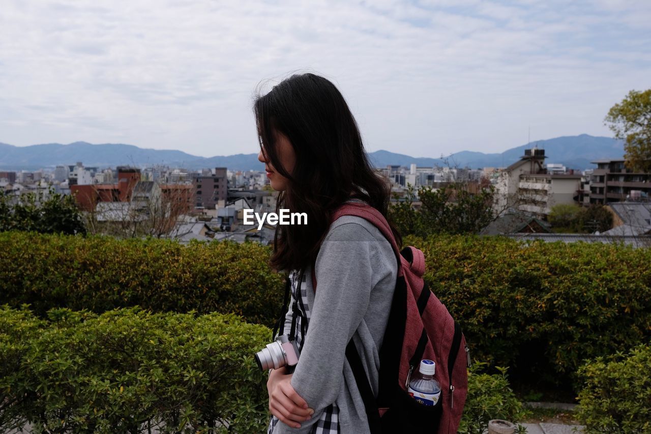 Side view of woman standing by cityscape against sky