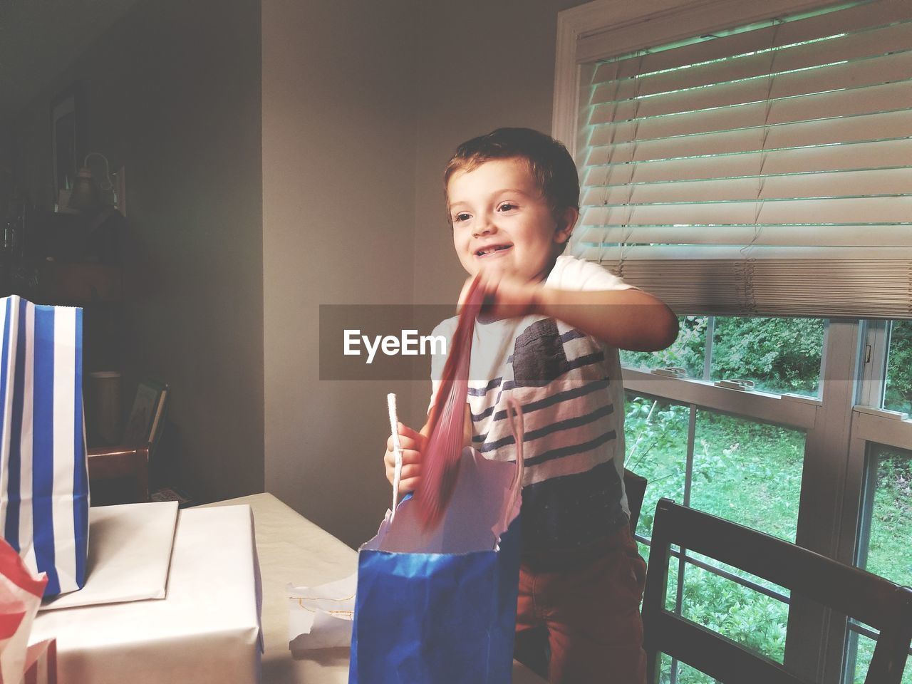 Cute boy looking away while holding bag at home