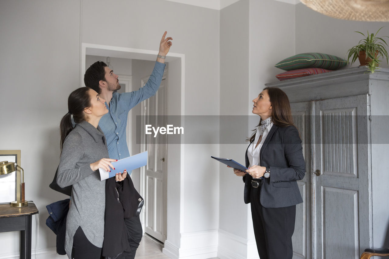 Woman and female realtor looking at man pointing up while standing in room