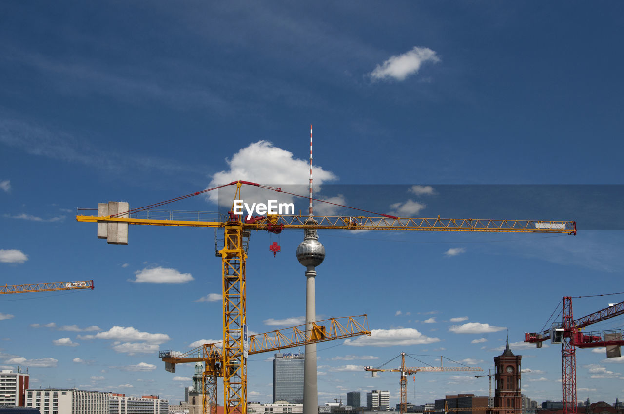 Fernsehturm and cranes against sky