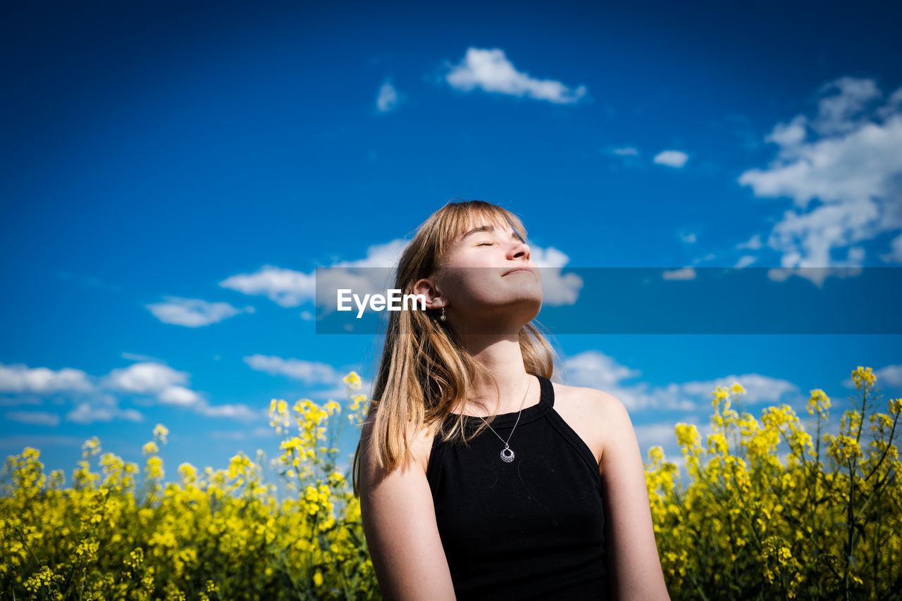 Low angle view of teenage girl with eyes closed sitting against blue sky