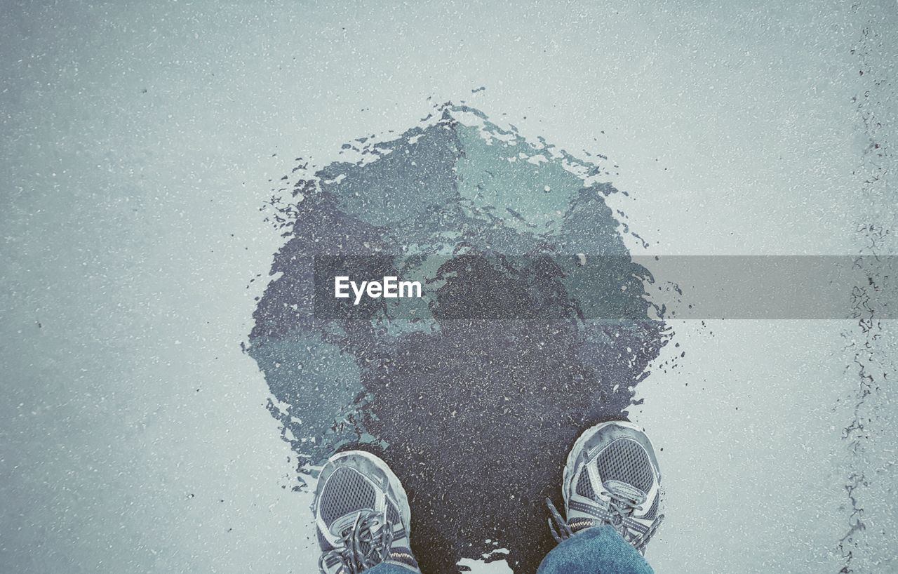 Low section reflection of man standing with umbrella in rain