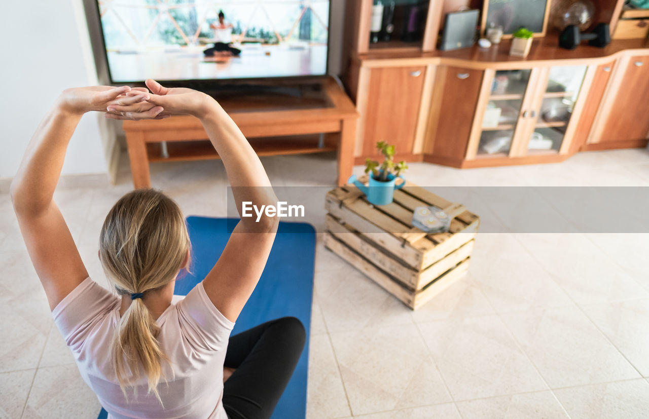 High angle view of woman with arms raised exercising at home