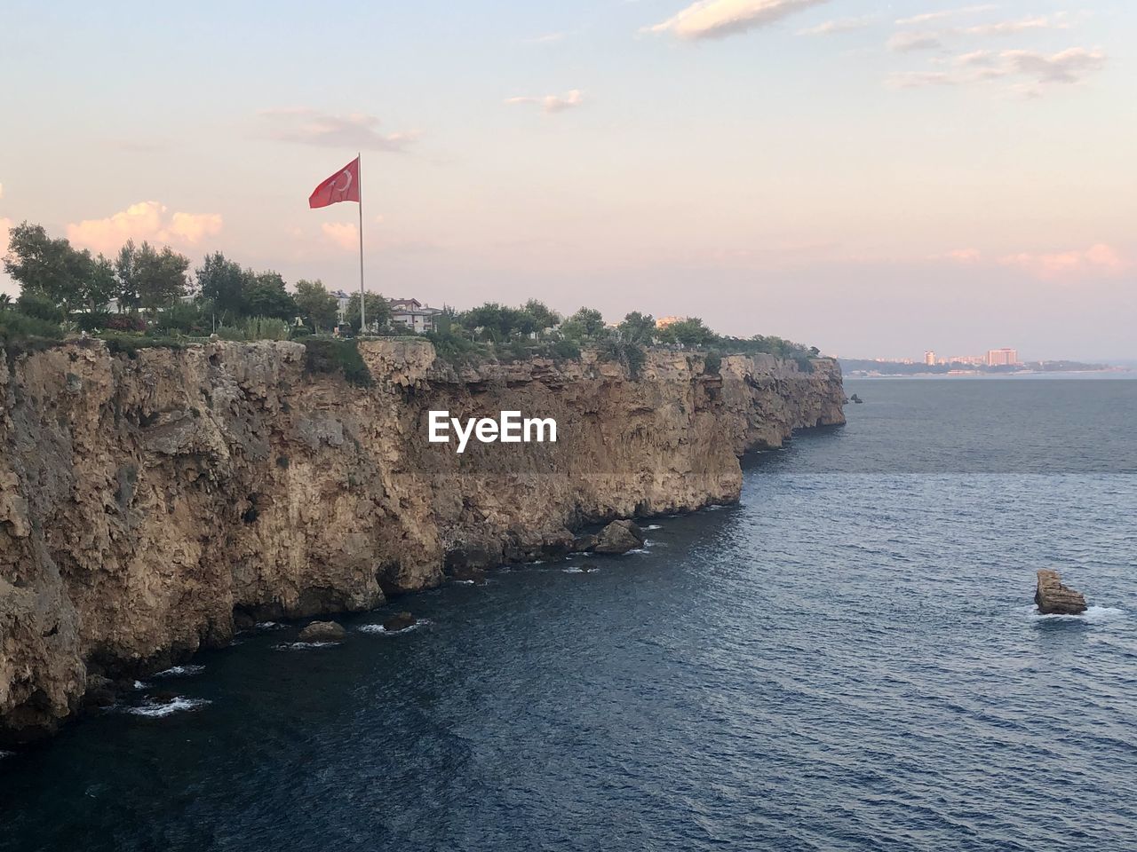 water, sea, coast, shore, sky, flag, ocean, rock, body of water, nature, bay, land, cliff, patriotism, scenics - nature, sunset, horizon, beauty in nature, wave, beach, terrain, no people, architecture, cloud, tranquility, environment, travel destinations, outdoors, tranquil scene, travel, built structure, tower, day, coastline, transportation, blue