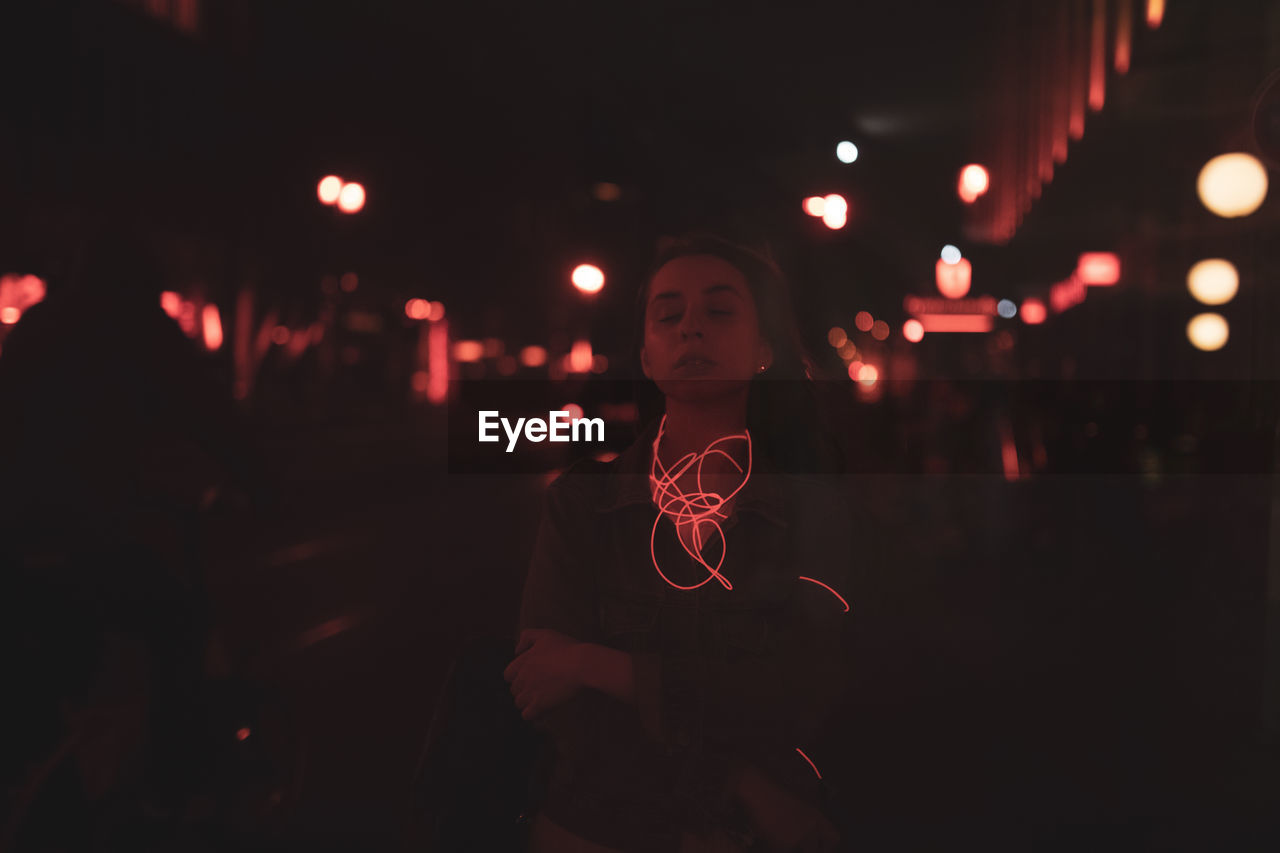 Full length portrait of woman standing against illuminated red lights at night