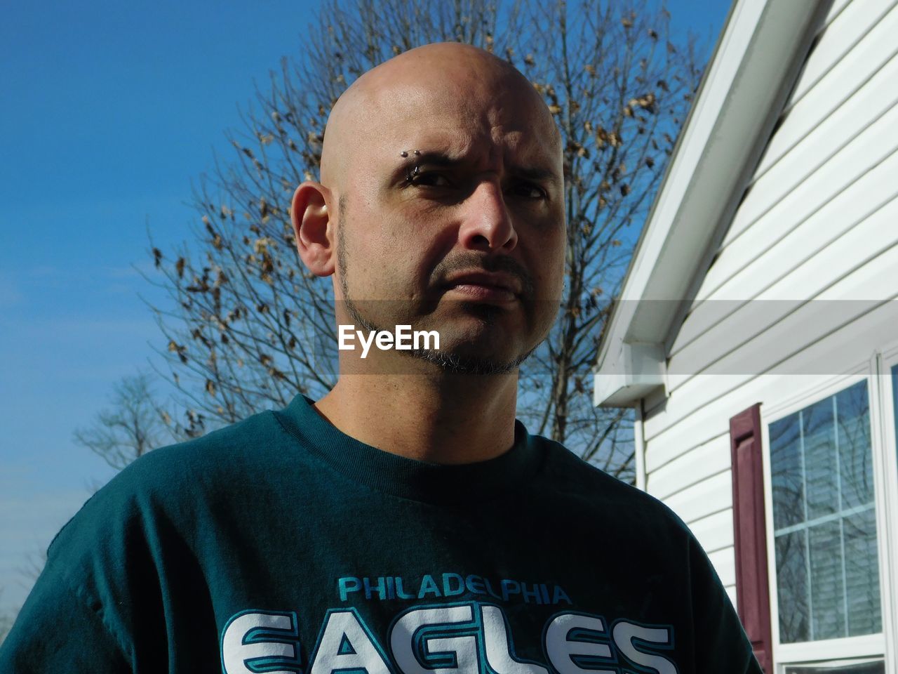 Low angle portrait of bald man by house during sunny day