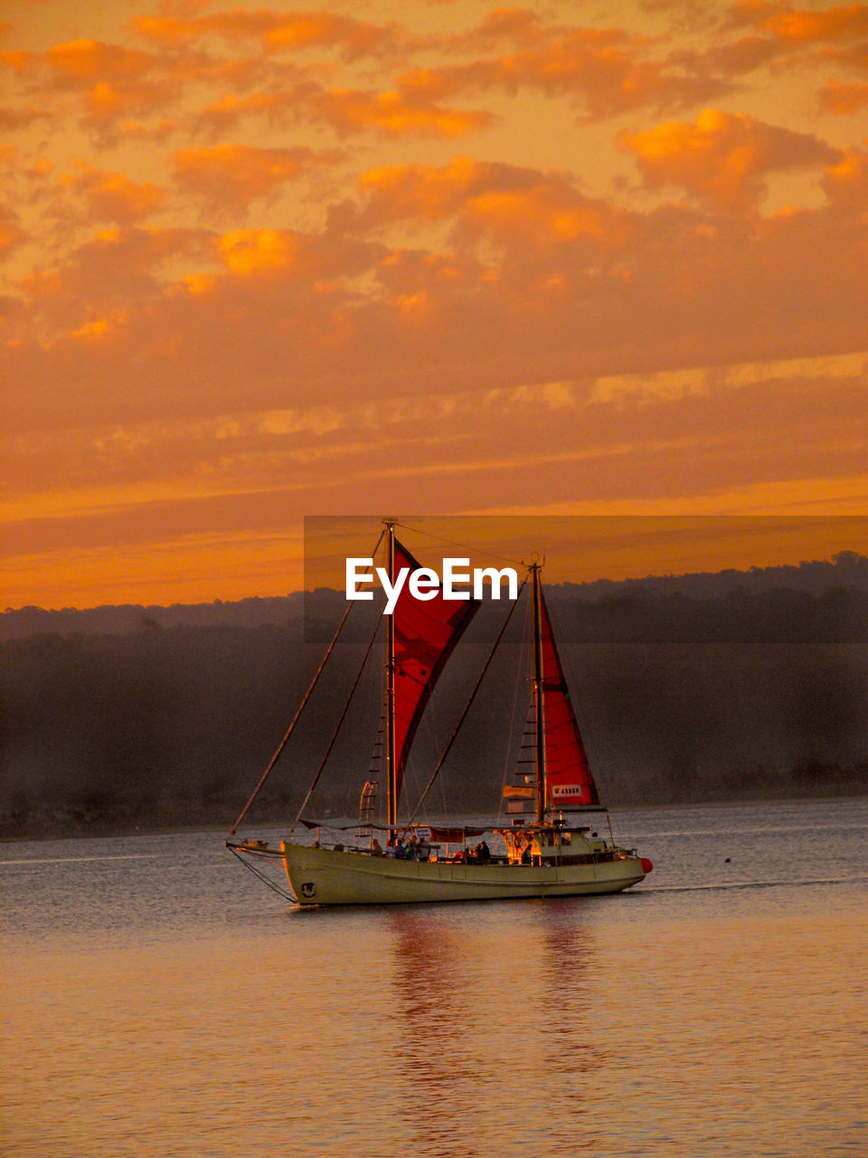 SAILBOATS SAILING ON SEA AGAINST ORANGE SKY