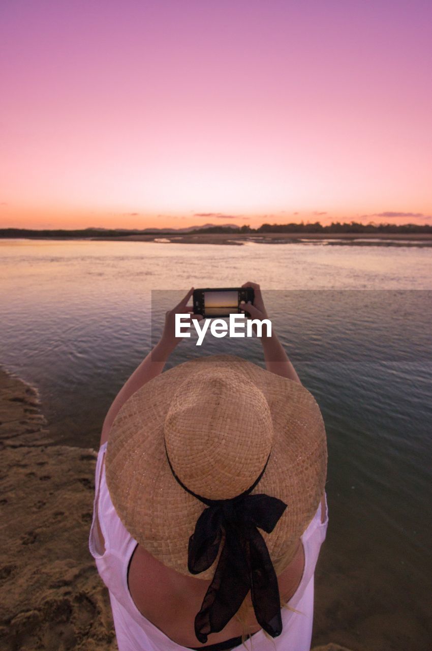 Rear view of woman photographing river during sunset