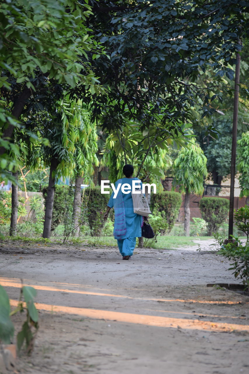 Rear view of woman walking on road by trees