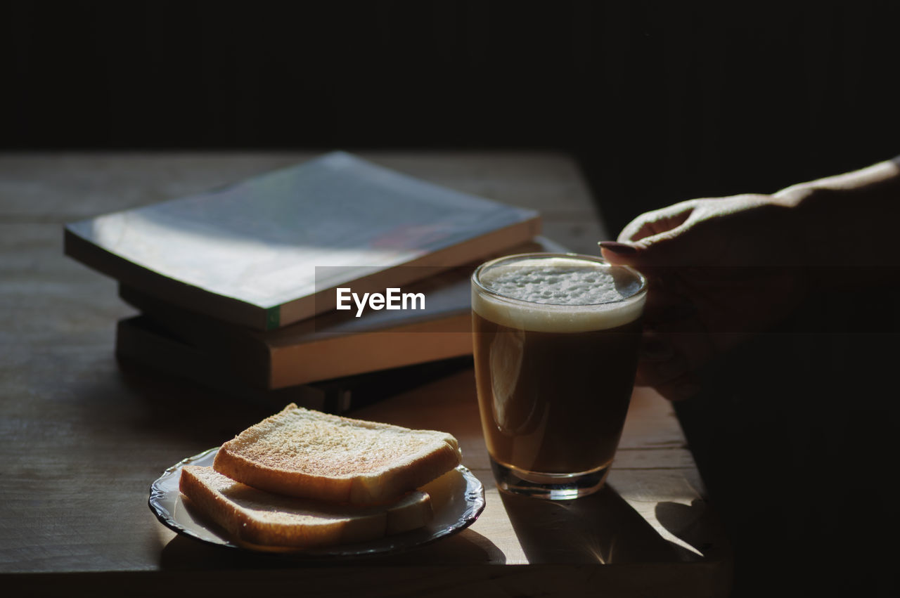 Close-up of hand holding coffee cup by toasted bread and books on table